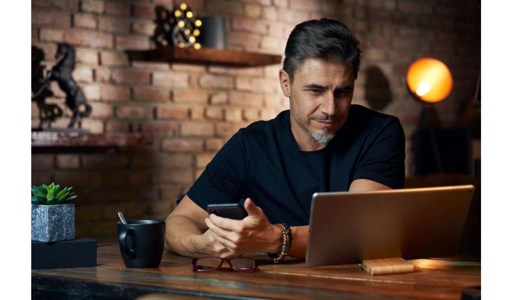 man on laptop holding phone