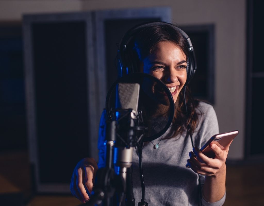 smiling woman in recording studio holding a phone recording for an audiobook