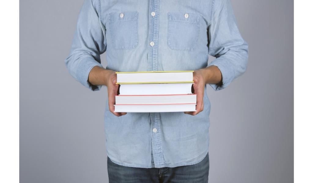 man holding multiple books in his hand planning to read more than one book at a time. 